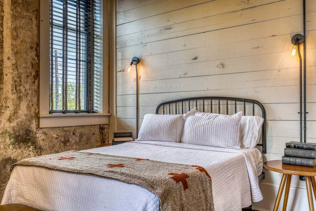 A cozy bedroom with a metal bed frame, wood-paneled walls, and vintage lighting, showcasing rustic charm and comfort.