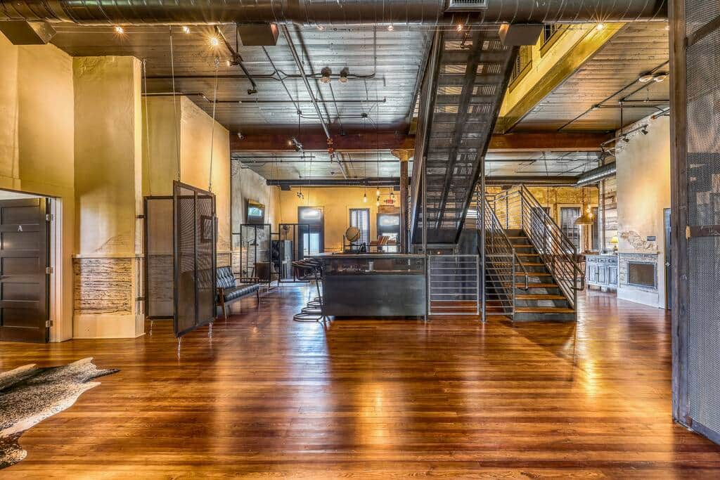 A large open space with wooden floors, a metal staircase, and exposed beams, reflecting a blend of industrial and rustic design.