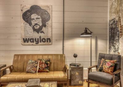 A lounge area with a leather couch, armchair, and a large wall art piece of Waylon Jennings, blending modern and vintage decor.