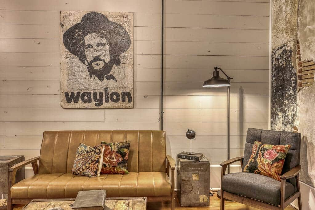 A lounge area with a leather couch, armchair, and a large wall art piece of Waylon Jennings, blending modern and vintage decor.