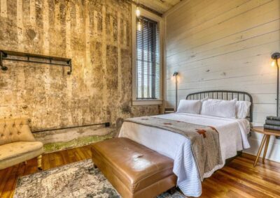 A cozy bedroom with a metal bed frame, wood-paneled walls, and vintage lighting, showcasing rustic charm and comfort.