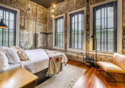 A cozy bedroom with exposed brick walls, large windows, and modern furnishings, reflecting the blend of old and new.