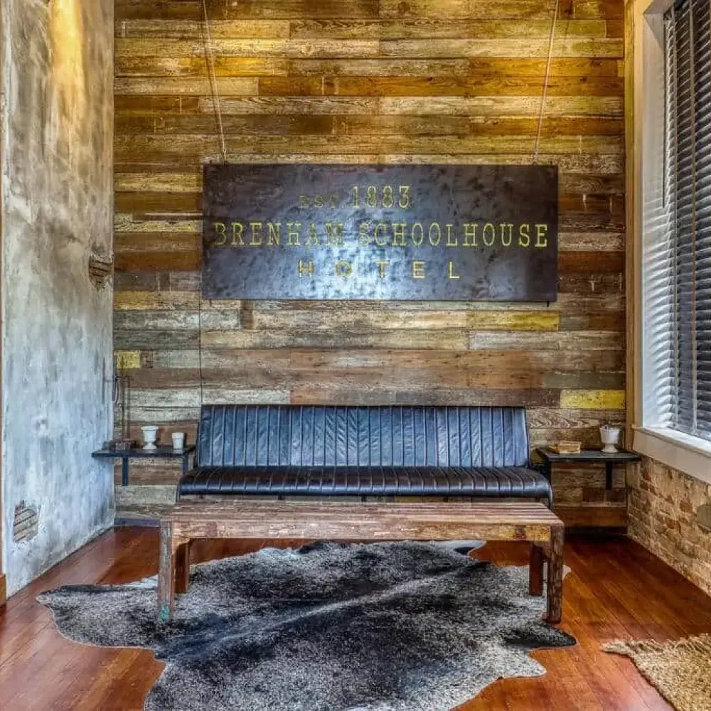 A rustic lobby with wooden walls and flooring, featuring a sign for the Brenham Schoolhouse Hotel, exuding vintage character.