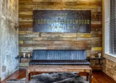 A rustic lobby with wooden walls and flooring, featuring a sign for the Brenham Schoolhouse Hotel, exuding vintage character.